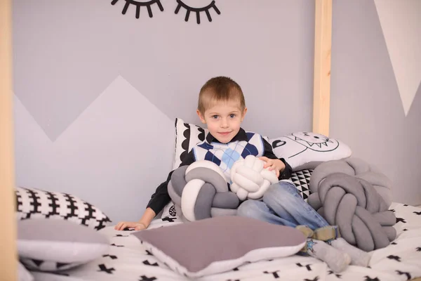 一个穿着休闲装的男孩躺在儿童房的床上 手里拿着一个装饰枕头 — 图库照片