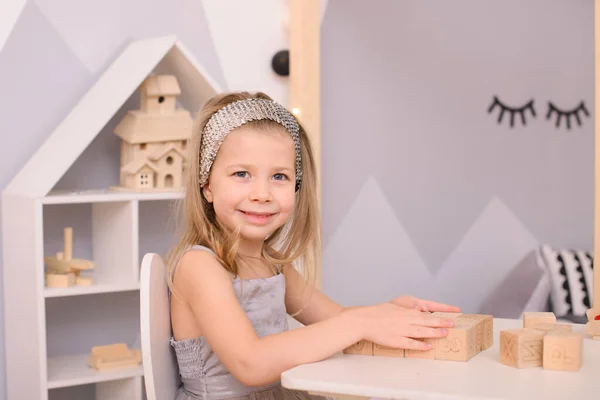 一个头发上有圈圈的女孩在儿童房里玩立方体游戏 她坐在并站在一张白色的桌子旁 — 图库照片