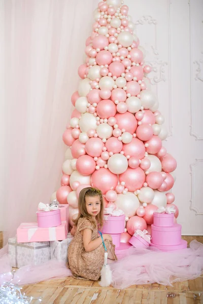 Ένα Όμορφο Κοριτσάκι Ένα Εορταστικό Φόρεμα Κάθεται Κοντά Ένα Χριστουγεννιάτικο — Φωτογραφία Αρχείου