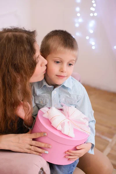 Mom Kisses Her Son Sitting Her Arms Holding Pink Gift — Stock Photo, Image