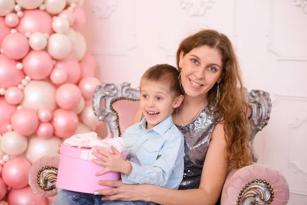 長い波状の髪を持つお母さん 彼女の腕の中で彼女の息子を保持し 白いリボンとピンクのギフトボックス — ストック写真