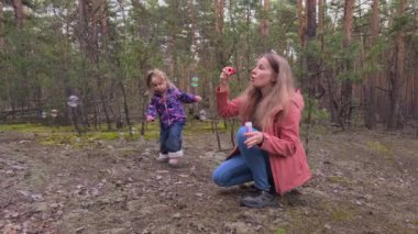 Mutlu genç anne ve kızı ormanda sabun köpüğü üflüyorlar..