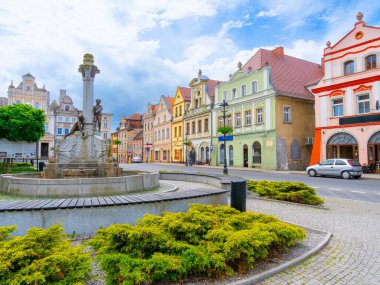 2024-05-31; Çekici bir kasaba meydanında bulunan tarihi çeşme ve arka planda klasik mimari, Gryfow Slaski, Polonya.