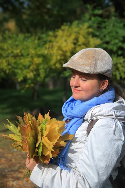 Fotoğraf, elinde sarı sonbahar yapraklarından bir buket olan genç ve güzel bir kadının portresini gösteriyor..