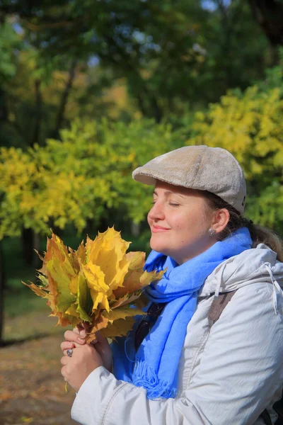 Fotoğrafta genç bir kadının portresi var. Taze sonbahar yapraklarının kokusundan zevk alıyor..