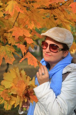 Fotoğraf, güneş gözlüklü, sarı akçaağaç yapraklı genç ve çekici bir kadının portresini gösteriyor..