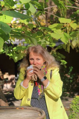 Fotoğrafta, sarı yağmurluklu genç bir kadın iştah açıcı bir şekilde sokak yemeği yiyor..