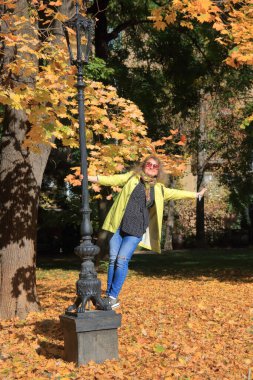 Fotoğraf Odessa şehrinde çekildi. Resimde, sarı yağmurluklu cana yakın bir kız bir sonbahar parkında sokak lambasının dibinde duruyor..