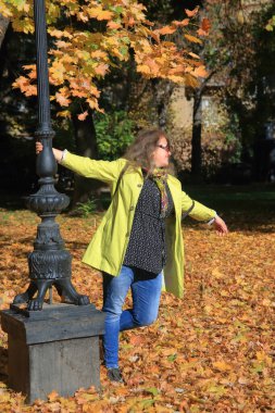 Fotoğraf Odessa Palais Royal adlı parkta çekildi. Sarı pelerinli genç bir kadın sonbahar portakal yaprakları arasında bir sokak lambasının etrafında dönüyor..