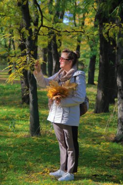 Fotoğraf Odessa Parkı 'nda çekildi. Dyukovsky Bahçesi. Resimde, bir buket sarı yapraklı genç bir kadın bir ağacın dallarındaki yaprakları inceliyor..