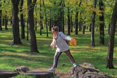 Fotoğrafta, genç bir kadın sonbahar ormanında taştan taşa zıplıyor..