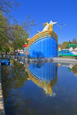 Çocuklar için şişirilebilir bir slayt Odessa 'daki bir şehir parkındaki bir göletin yüzeyinden yansıyor..