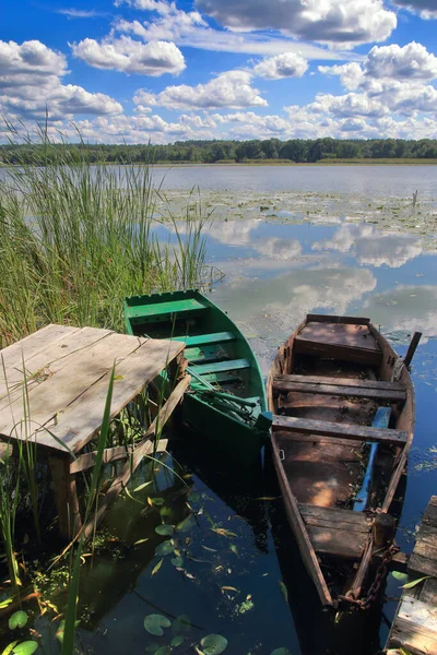 The photo was taken in Ukraine, on the river Southern Bug. The picture shows a fishing boat moored near the river bank under a blue sky with light clouds reflected in the water.
