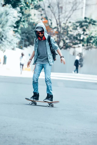 スケートボードに乗って音楽を聴く幸せな10代の男の子 ストリートスタイルの衣装 積極的なライフスタイル 現代の青少年文化 — ストック写真