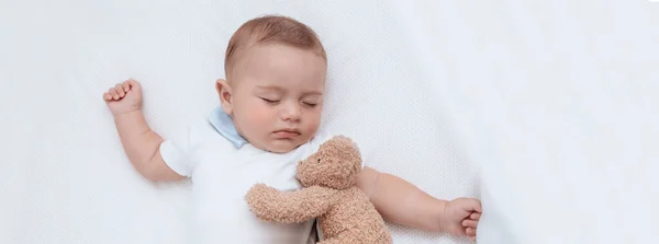 彼の親友の柔らかいおもちゃのクマと彼のベッドで滑り素敵な小さな赤ちゃんの少年の肖像画 幸せな子供時代 — ストック写真