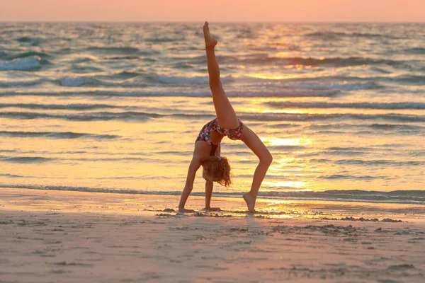 夕焼け空を背景にビーチでヨガをする甘い女の子 積極的な夏のキャンプ 屋外で踊る 健康な子供時代 — ストック写真