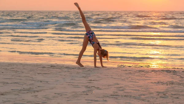 夕日の空を背景にビーチでスポーツの練習をしているかなり10代の女の子 積極的な夏のキャンプ 海の近くで踊る 健康な子供時代 — ストック写真