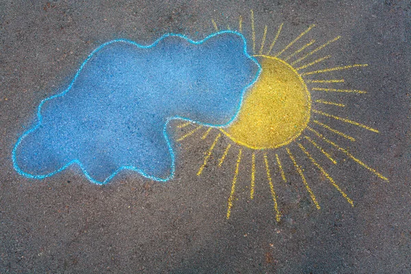 Beautiful abstract background. Hand drawing chalk picture on asphalt of a yellow sun and blue cloud. Conceptual photo of peace in Ukraine.
