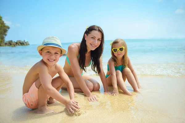 ビーチで砂の城を作る2人の幸せな子供を持つ若い母親 幸せな家族はビーチリゾートで夏休みを過ごしています 旅する人 — ストック写真