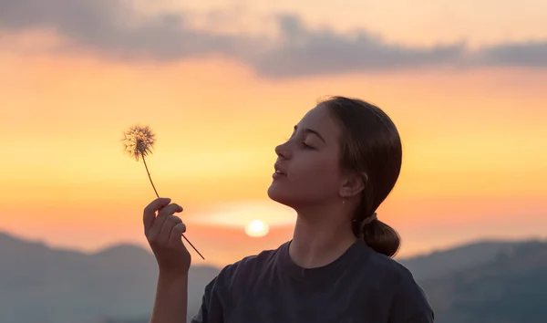 山の中の美しい夕日の空に素敵な10代の女の子の肖像画 タンポポの花を楽しんで吹いています 願い事をする 活発な十代の若者たち — ストック写真