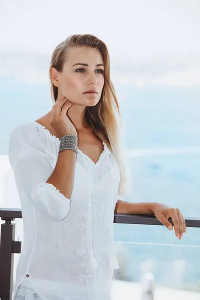 Portrait of a beautiful girl dressing in white dress relaxing on the balcony. Gentle authentic woman look. Happy healthy life.