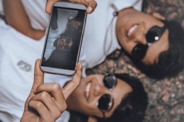 Güneş gözlüğü takan iki genç adam, mutlu bir şekilde gülümsüyor, o anın hatırlanmaya değer bir fotoğrafını çekiyor, dostluk, duygular ve güneşli bir gün..