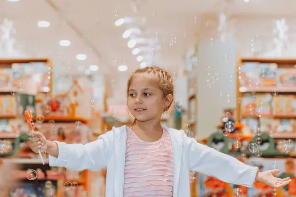 可爱的小女孩快乐地在美丽的大玩具店里吹泡泡肥皂 快乐的孩子在购物中心里玩得很开心 她眼中的快乐 — 图库照片