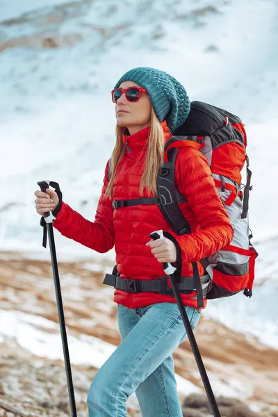 A young girl with long hair is engaged in winter tourism in the snowy mountains. Walking poles help her overcome snow-covered mountain slopes.