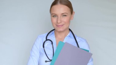 Genç bir doktorun FHD videosu elinde hastalarının tıbbi kayıtlarını tutuyor. Gülümsemesi ve pozitifliği hızlı bir iyileşmeye katkıda bulunuyor. Ağır çekim. 1920x1080.