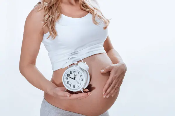 妊娠中の少女は まもなく赤ん坊を産むだろうと言っているかのように 丸い警報を鳴らしています 身体の一部 白い背景に孤立した ロイヤリティフリーのストック写真