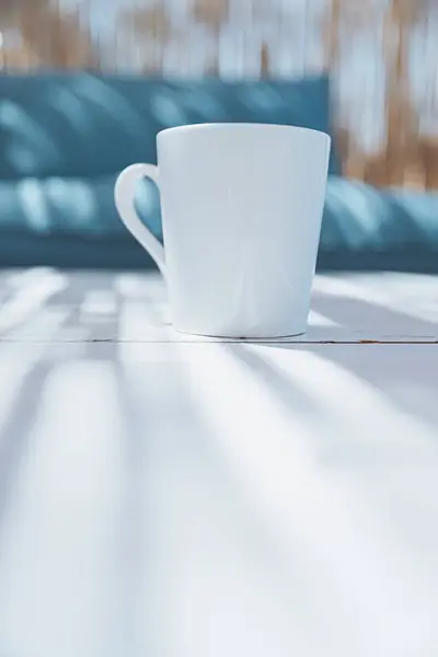 A white cup with a morning drink stands on the table of a summer bungalow next to a blue sofa. Cozy summer house at the resort. Summer vibe concept.