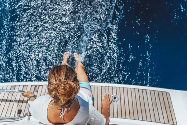漂亮的女性坐在帆船甲板上欣赏大海的美景 在海滩度过暑假 健康快乐的生活方式 图库照片