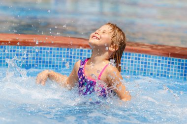 Havuza su sıçratan mutlu küçük bir kızın portresi. Tatilleri plaj merkezinde geçirmek. Yaz tatili. Bebek turist eğleniyor.