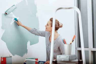 Yeni dairesinde boya silindiri kullanarak duvar boyayan mutlu genç bir kadının fotoğrafı. Kozmetik tamiri yapıyor. Hayatta yeni bir aşama kavramı.