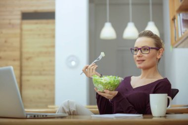 Genç ve neşeli bir kadın sebze salatası şeklinde bir porsiyon vitamin alıyor. İş yerinde günün ortasında sağlıklı bir yemek. Ofisteki insanlar..
