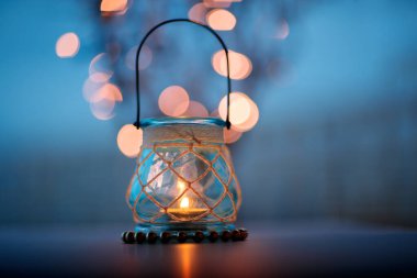 Büyüleyici Bokeh ışıklarıyla çevrili cam fenerde parlayan güzel bir mum hoş bir atmosfer yaratır. Düğün masası dekoru