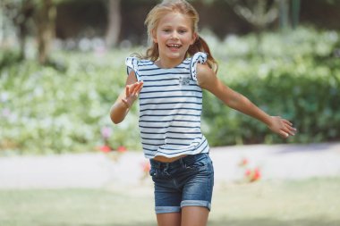 Neşeli ve mutlu bir kız açık havada güzel güneşli bir günün tadını çıkarıyor, şık bir şekilde çizgili bluz ve kot şort giyiyor. Çocuk modası. Model Çocuk.
