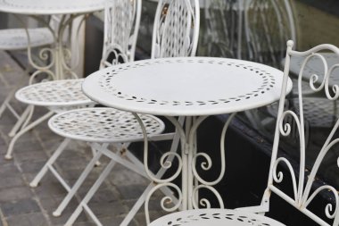Açık bir kafe veya restoranda sandalye ve masalar boş duruyor ve misafirleri bekliyor..