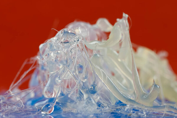 На кусочке синего картона на красном фоне можно увидеть уже охлажденные капли и нити горячего клея