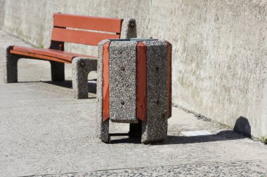 Polonya 'nın Gdynia kentindeki kaldırımda beton bir duvarın yanında beton bir çöp tenekesi ve bir bank bulunmaktadır.