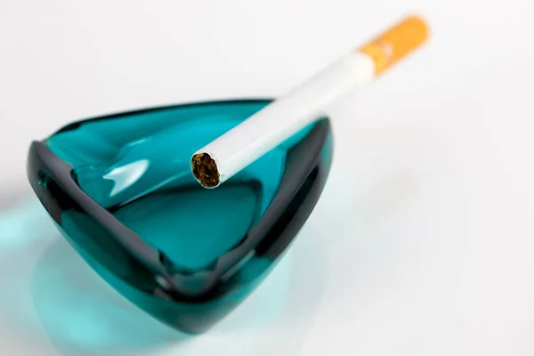 ガラス灰皿の端には1本のライトのないタバコが置かれています タバコを吸うか健康的なライフスタイルを選ぶかどうか疑問に思うかもしれません — ストック写真