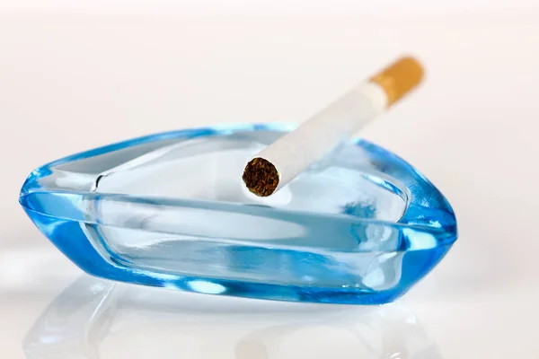 ガラス灰皿の端には1本のライトのないタバコが置かれています タバコを吸うか健康的なライフスタイルを選ぶかどうか疑問に思うかもしれません — ストック写真