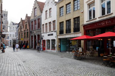 Bruges, Belçika - 13 Eylül 2022: Trafik olmayan asfalt bir caddenin kaldırımında birkaç kişi. Geleneksel tuğla evler cadde boyunca..