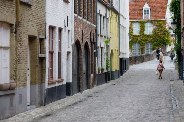 Bruges, Belçika - 10 Eylül 2022 Dar asfalt bir sokakta tuğla evler. Bu evlerin cepheleri çeşitli renklerle boyandı.