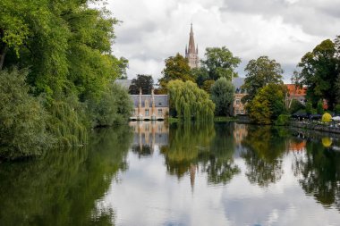 Bruges, Belçika - 11 Eylül 2022: Şehrin güneyindeki ünlü Minnewater Gölü 'nün olduğu güzel bir parkta manzara. Kilise kulesi ve diğer tuğla binalar biraz daha görünür.