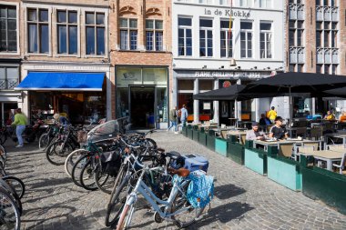 Bruges, Belçika - 8 Eylül 2022: Bisikletler tuğla evlerin yanındaki kaldırım taşı meydanında park edilmiş, ve yakınlardaki açık hava restoranında hala yerler var. Burada da birkaç kişi var.