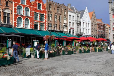 Bruges, Belçika - 8 Eylül 2022: Renkli tuğlalı evler Pazar Meydanı 'nın önünü oluşturur. Ayrıca üzerinde yeşil, kırmızı ve siyah şemsiyeler olan büyüleyici sokak kafeleri de var.