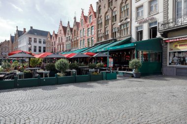 Bruges, Belçika - 8 Eylül 2022: Renkli tuğlalı evler Pazar Meydanı 'nın önünü oluşturur. Ayrıca üzerinde yeşil, kırmızı ve siyah şemsiyeler olan büyüleyici sokak kafeleri de var.