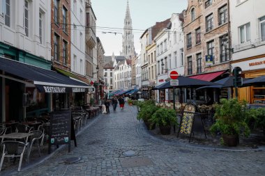 Brussels, Belgium - September 16, 2022: A narrow paved street with outdoor cafes and restaurants on both sides. In the distance is the City Hall towe