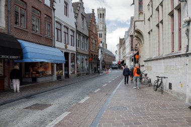 Bruges, Belgium - September 8, 2022: A narrow cobbled street that leads between traditional houses towards the famous belfry, visible here in the distance